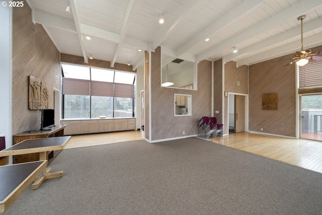 unfurnished living room featuring wooden walls, plenty of natural light, beamed ceiling, ceiling fan, and wood finished floors