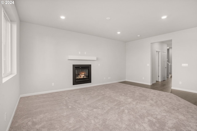 unfurnished living room with recessed lighting, a glass covered fireplace, dark carpet, and baseboards