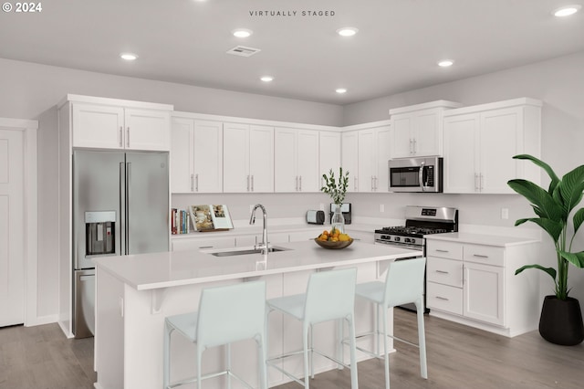 kitchen with stainless steel appliances, white cabinets, a sink, an island with sink, and light wood-type flooring