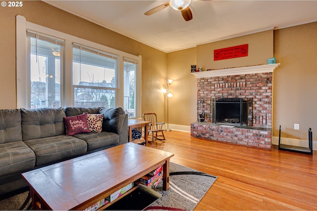 living area featuring ceiling fan, wood finished floors, baseboards, ornamental molding, and a brick fireplace