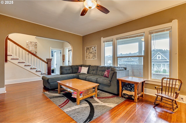 living room with arched walkways, stairway, ornamental molding, wood finished floors, and baseboards