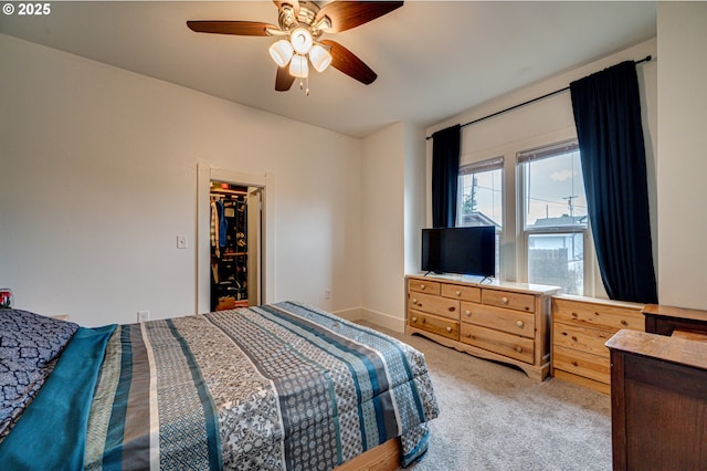 bedroom with ceiling fan, baseboards, a walk in closet, and light colored carpet