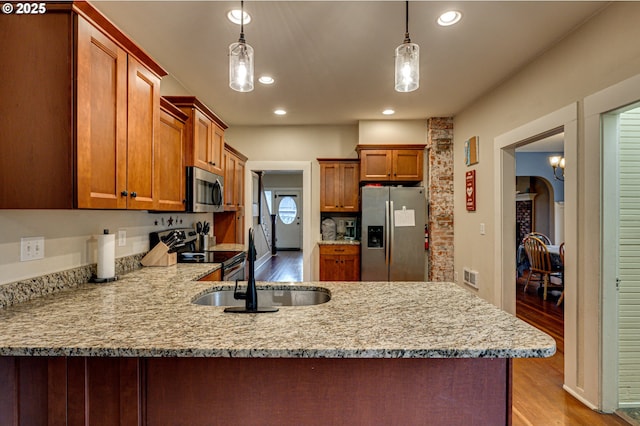 kitchen featuring stainless steel appliances, a peninsula, a sink, light wood-style floors, and hanging light fixtures