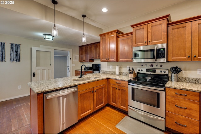 kitchen with stainless steel appliances, brown cabinetry, a peninsula, and a sink