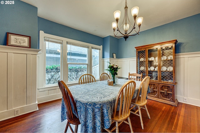 dining space featuring a wainscoted wall, a decorative wall, dark wood finished floors, and a notable chandelier