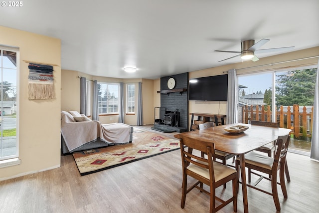 dining room with a wood stove, light wood-style flooring, and a ceiling fan