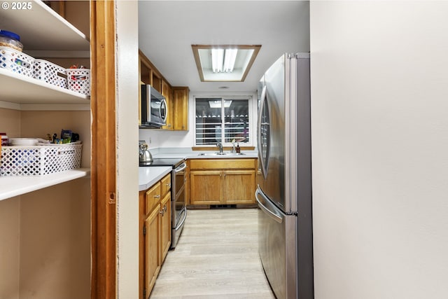 kitchen featuring light wood-style flooring, brown cabinets, stainless steel appliances, light countertops, and a sink