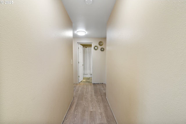 hall with light wood-style flooring and a textured wall