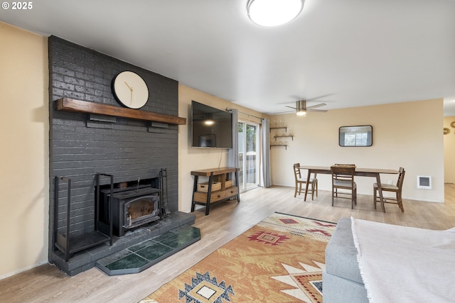 living room featuring baseboards, visible vents, a ceiling fan, wood finished floors, and a wood stove