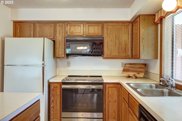 kitchen featuring stainless steel range with electric cooktop, light countertops, a sink, freestanding refrigerator, and black microwave
