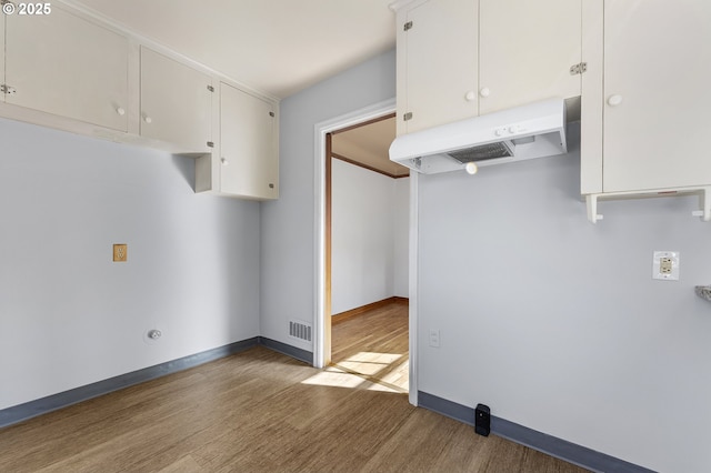 kitchen with white cabinets, under cabinet range hood, baseboards, and wood finished floors