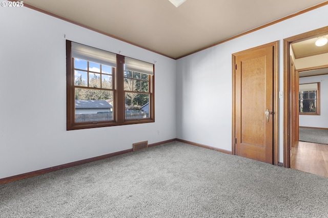 spare room with carpet floors, baseboards, visible vents, and crown molding