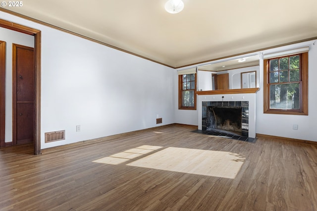 unfurnished living room with ornamental molding, a tile fireplace, visible vents, and wood finished floors