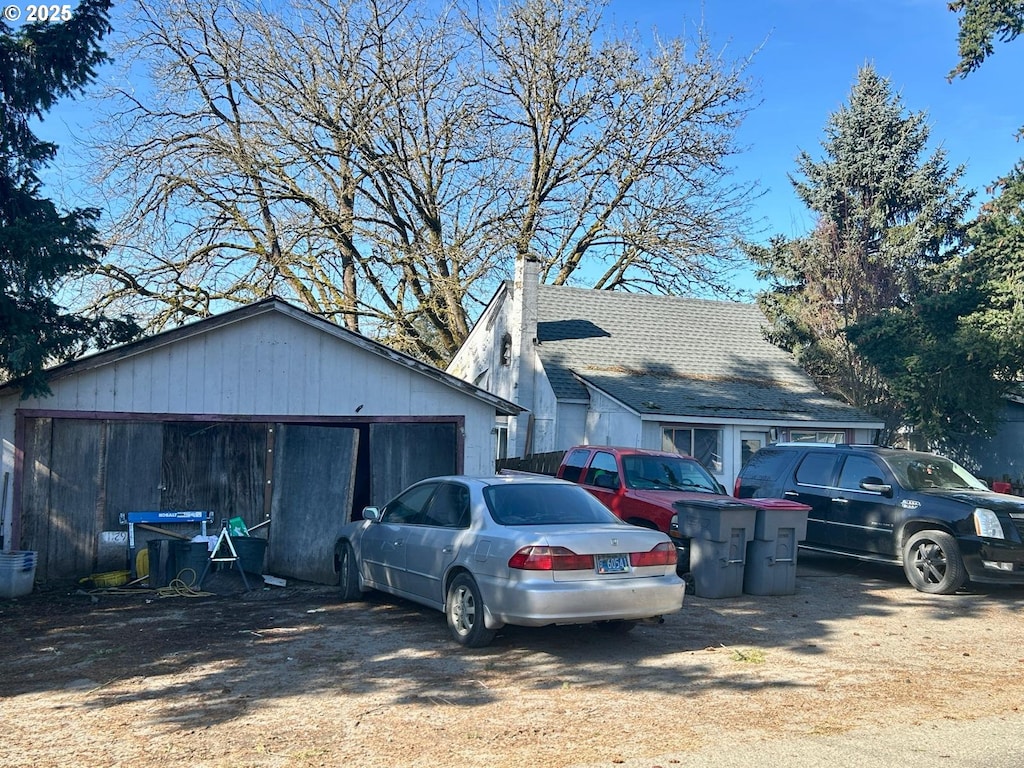 view of property exterior featuring a shingled roof, a detached garage, a chimney, and an outdoor structure