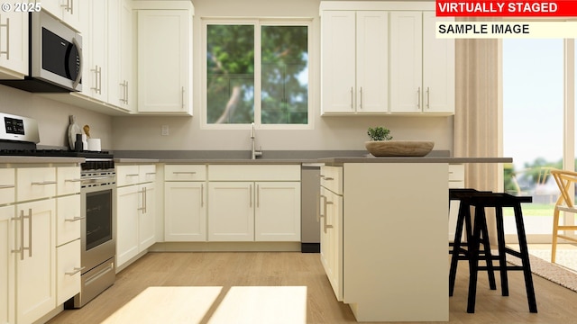 kitchen featuring sink, light hardwood / wood-style flooring, stainless steel appliances, white cabinets, and a kitchen bar