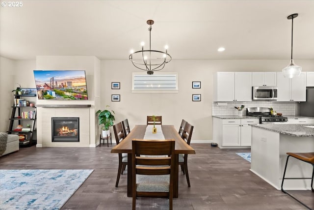 dining room featuring recessed lighting, a notable chandelier, dark wood-type flooring, baseboards, and a glass covered fireplace