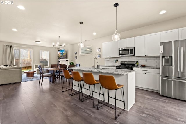 kitchen featuring dark wood-style floors, appliances with stainless steel finishes, open floor plan, a sink, and backsplash