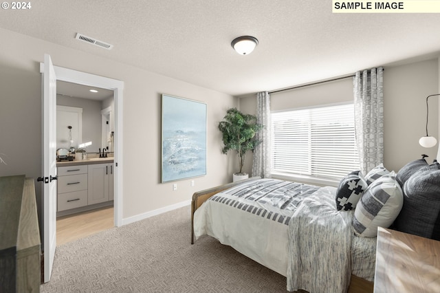 bedroom with a textured ceiling, light colored carpet, connected bathroom, and sink