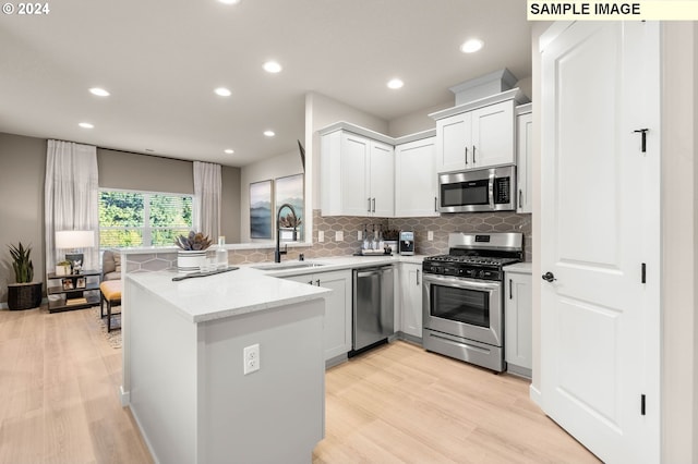 kitchen featuring appliances with stainless steel finishes, light wood-type flooring, kitchen peninsula, white cabinets, and sink