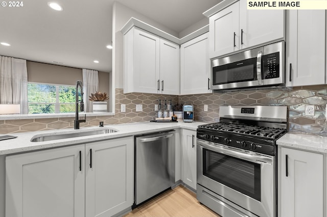 kitchen with stainless steel appliances, sink, white cabinetry, backsplash, and light stone countertops