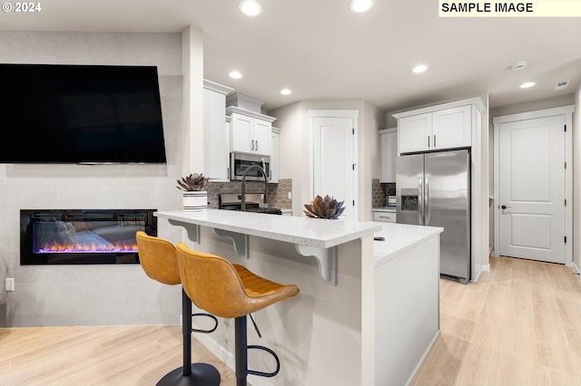 kitchen featuring appliances with stainless steel finishes, a breakfast bar, light hardwood / wood-style flooring, and white cabinets