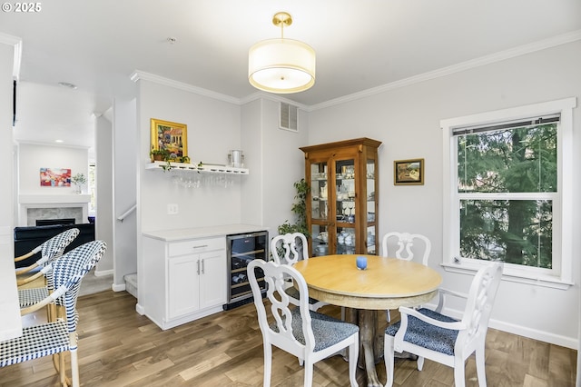 dining area with visible vents, a fireplace, ornamental molding, wine cooler, and light wood-type flooring