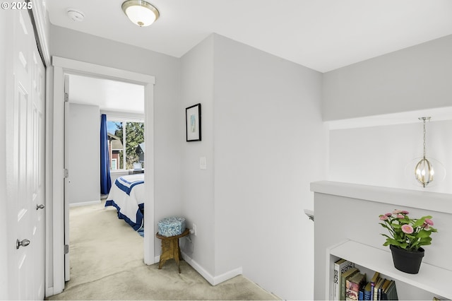 hallway with a chandelier, light colored carpet, and baseboards