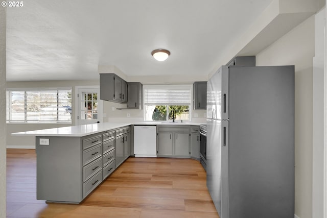 kitchen featuring sink, light wood-type flooring, appliances with stainless steel finishes, gray cabinets, and kitchen peninsula