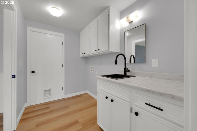 laundry area featuring sink, hookup for a washing machine, light hardwood / wood-style floors, and cabinets