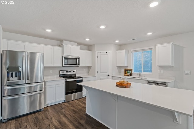 kitchen with appliances with stainless steel finishes, sink, white cabinets, dark hardwood / wood-style flooring, and a center island