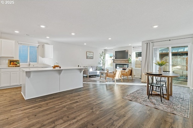 kitchen with a breakfast bar, a kitchen island, dark hardwood / wood-style floors, a textured ceiling, and white cabinets