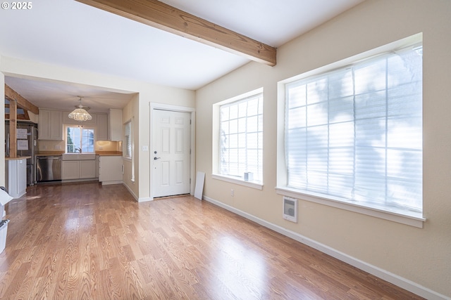 unfurnished living room with beamed ceiling, baseboards, healthy amount of natural light, light wood finished floors, and heating unit