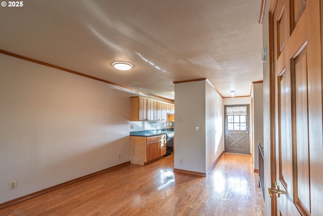 kitchen with crown molding, dark countertops, light wood-style floors, a sink, and baseboards