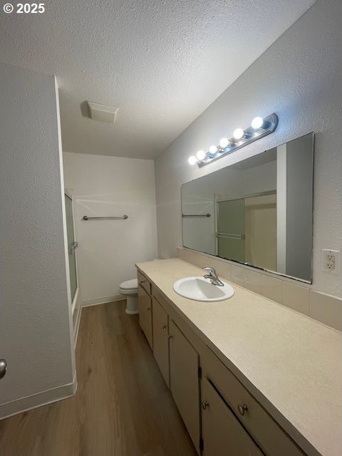 755735 Bluff Ave, Bandon, OR 97411 - full bathroom featuring wood finished floors, toilet, vanity, combined bath / shower with glass door, and baseboards