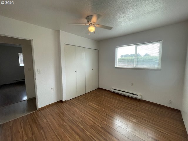 755735 Bluff Ave, Bandon, OR 97411 - unfurnished bedroom featuring a baseboard heating unit, wood finished floors, a closet, baseboard heating, and ceiling fan