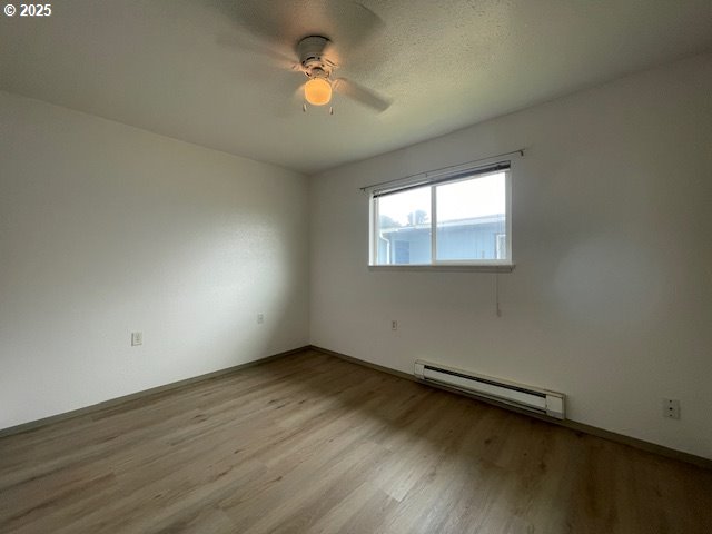 755735 Bluff Ave, Bandon, OR 97411 - empty room featuring a baseboard radiator, wood finished floors, ceiling fan, and baseboards