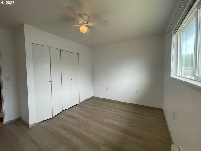 755735 Bluff Ave, Bandon, OR 97411 - unfurnished bedroom with wood finished floors, a closet, a ceiling fan, and a baseboard heating unit
