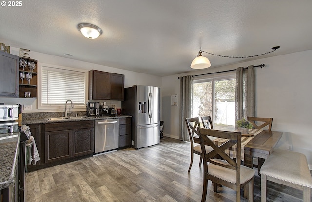 kitchen featuring sink, dark stone counters, light hardwood / wood-style floors, stainless steel appliances, and a textured ceiling