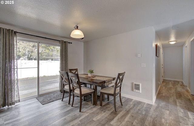 dining room featuring heating unit, light hardwood / wood-style flooring, and a textured ceiling