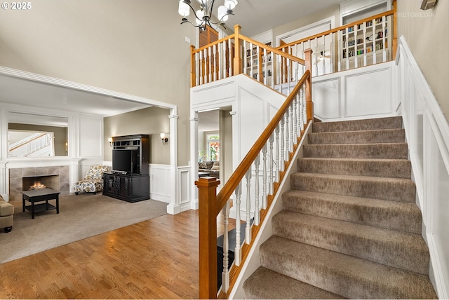 stairs featuring a notable chandelier, a decorative wall, a tiled fireplace, wood finished floors, and ornate columns