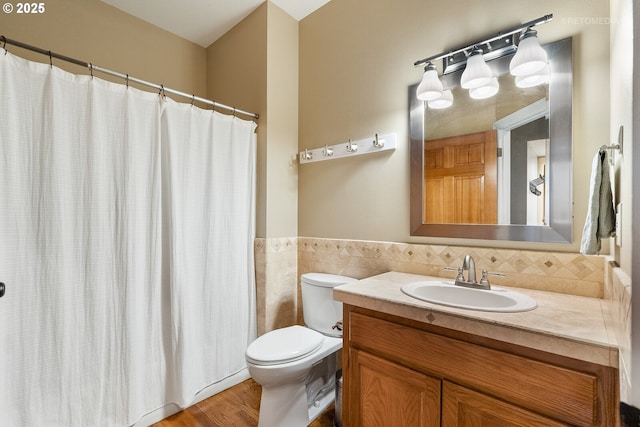 bathroom featuring a wainscoted wall, tile walls, toilet, vanity, and wood finished floors