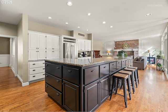 kitchen featuring white cabinets, a spacious island, stainless steel refrigerator, light wood-style floors, and a kitchen bar