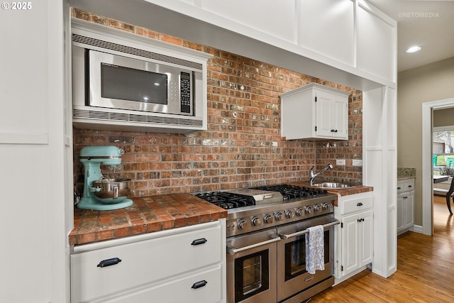 kitchen with stainless steel appliances, tile counters, light wood-style flooring, white cabinets, and a sink