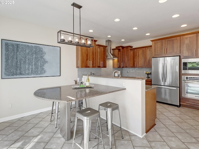 kitchen featuring stainless steel appliances, wall chimney exhaust hood, recessed lighting, tasteful backsplash, and brown cabinetry