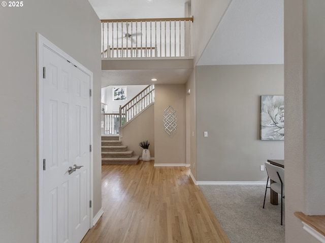 entryway with light wood-style floors, a high ceiling, stairs, and baseboards