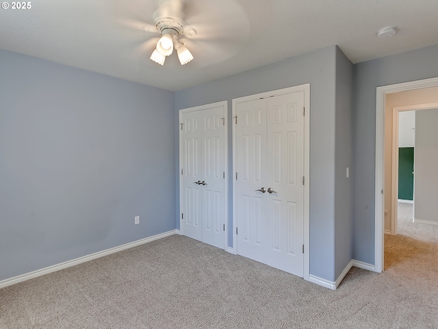 unfurnished bedroom featuring carpet, multiple closets, baseboards, and a ceiling fan