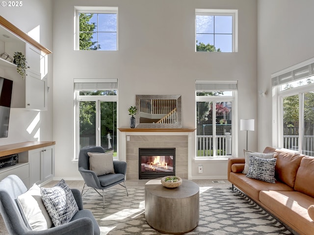 carpeted living room featuring a towering ceiling, a tiled fireplace, baseboards, and healthy amount of natural light