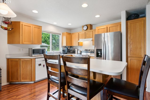 19030 SW Pike Ln, Beaverton, OR 97078 - kitchen with appliances with stainless steel finishes, under cabinet range hood, light wood-type flooring, a kitchen bar, and light countertops