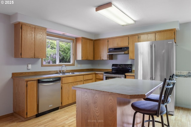 kitchen featuring appliances with stainless steel finishes, a sink, under cabinet range hood, light wood-type flooring, and a breakfast bar