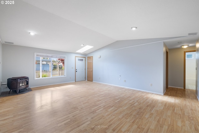 unfurnished living room with a wood stove, light wood-style floors, lofted ceiling, baseboards, and a skylight